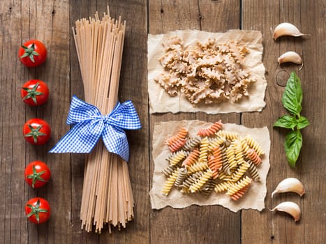 Pasta, tomatoes, garlic and basil on wooden background