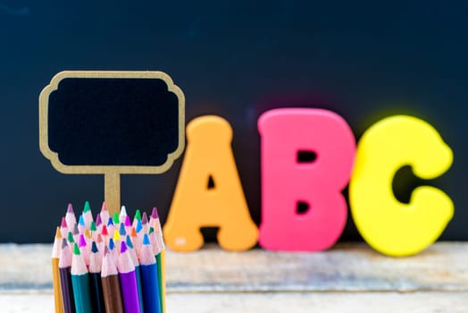 Wooden mini blackboard label and colouring pencils over chalkboard background and table with letters ABC, copy space available, education concept