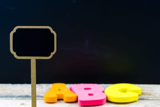 Wooden mini blackboard label over chalkboard background and table with letters ABC, copy space available, education concept