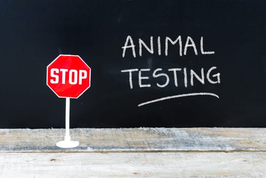 Mini STOP sign over chalkboard background and table, STOP ANIMAL TESTING concept