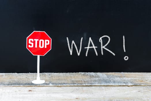 Mini STOP sign over chalkboard background and table, STOP WAR concept
