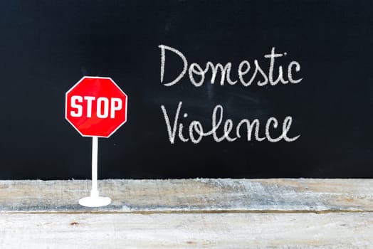 Mini STOP sign over chalkboard background and table, STOP DOMESTIC VIOLENCE concept