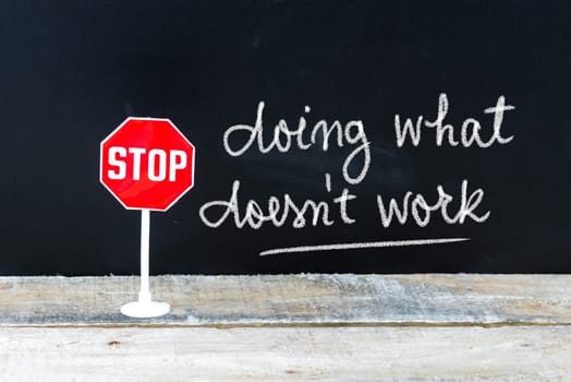 Mini STOP sign over chalkboard background and table, STOP DOING WHAT DOES NOT WORK concept