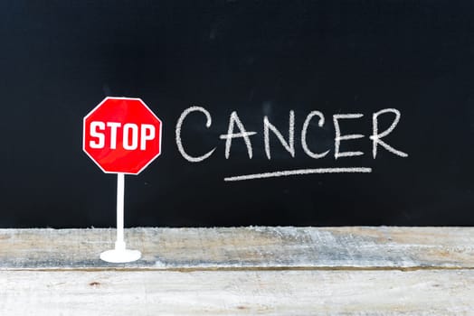 Mini STOP sign over chalkboard background and table, STOP CANCER concept