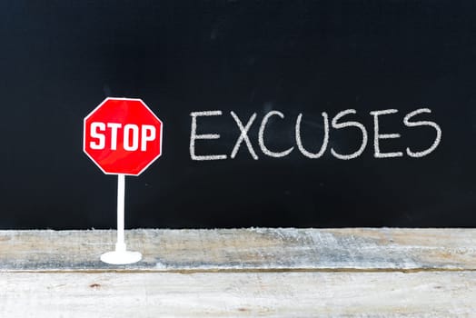 Mini STOP sign over chalkboard background and table, STOP EXCUSES concept