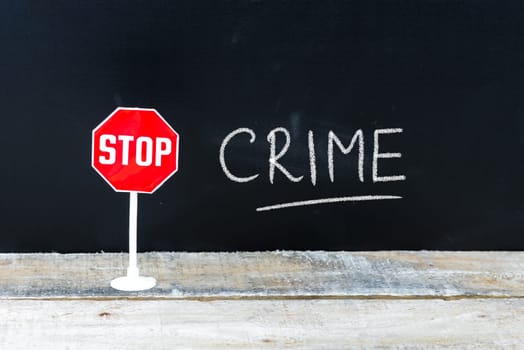 Mini STOP sign over chalkboard background and table, STOP CRIME concept