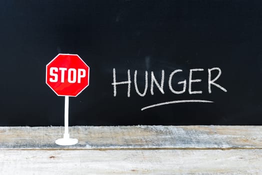 Mini STOP sign over chalkboard background and table, STOP HUNGER concept