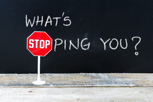 Mini STOP sign over chalkboard background and table, WHAT IS STOPPING YOU concept