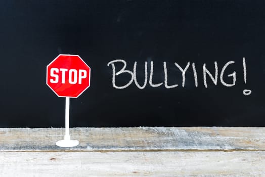 Mini STOP sign over chalkboard background and table, STOP BULLYING concept