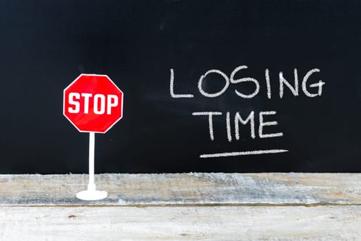 Mini STOP sign over chalkboard background and table, STOP LOSING TIME concept