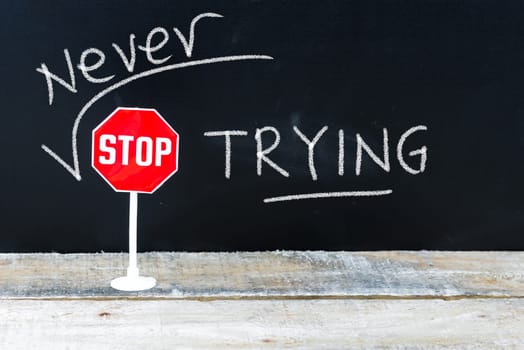 Mini STOP sign over chalkboard background and table, NEVER STOP TRYING concept
