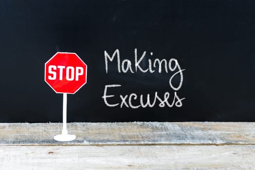 Mini STOP sign over chalkboard background and table, STOP MAKING EXCUSES concept