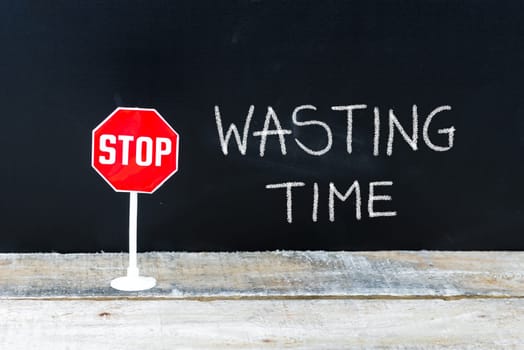 Mini STOP sign over chalkboard background and table, STOP WASTING TIME concept