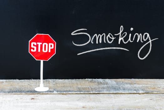 Mini STOP sign over chalkboard background and table, STOP SMOKING concept