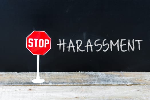 Mini STOP sign over chalkboard background and table, STOP HARASSMENT concept