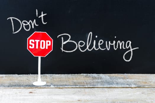 Mini STOP sign over chalkboard background and table, DO NOT STOP BELIEVING concept
