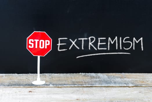 Mini STOP sign over chalkboard background and table, STOP EXTREMISM concept