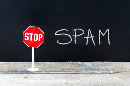 Mini STOP sign over chalkboard background and table, STOP SPAM concept