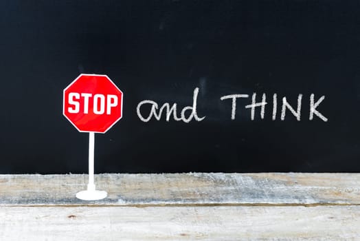 Mini STOP sign over chalkboard background and table, STOP and THINK concept