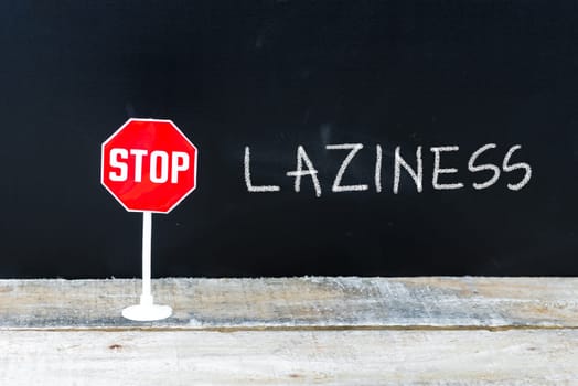 Mini STOP sign over chalkboard background and table, STOP LAZINESS concept