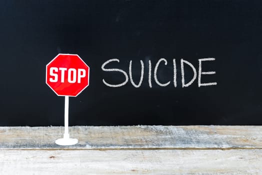 Mini STOP sign over chalkboard background and table, STOP SUICIDE concept
