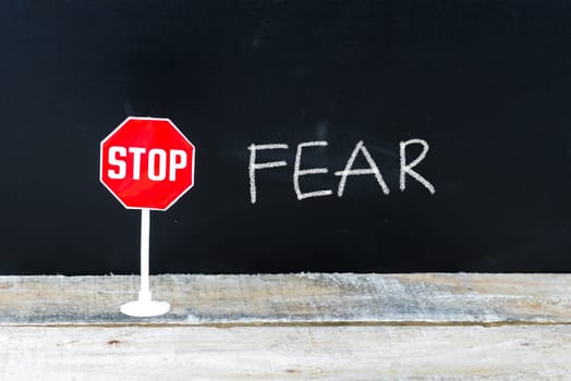 Mini STOP sign over chalkboard background and table, STOP FEAR concept