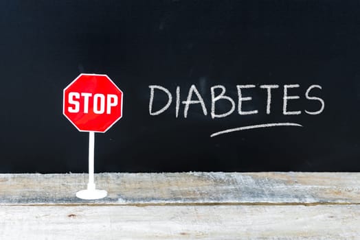 Mini STOP sign over chalkboard background and table, STOP DIABETES concept