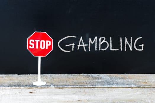Mini STOP sign over chalkboard background and table, STOP GAMBLING concept
