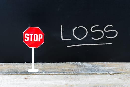 Mini STOP sign over chalkboard background and table, STOP LOSS concept