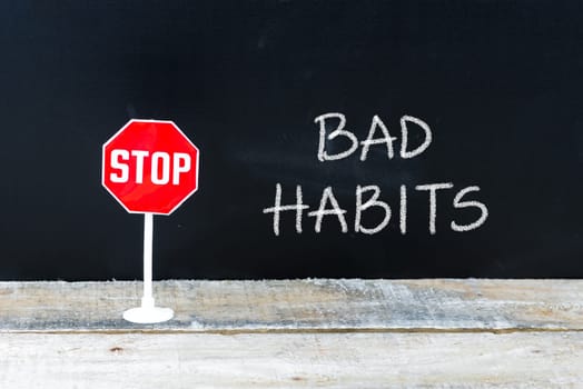 Mini STOP sign over chalkboard background and table, STOP BAD HABITS concept