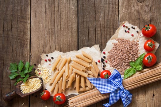 Pasta, tomatoes, basil and parsley on wooden background