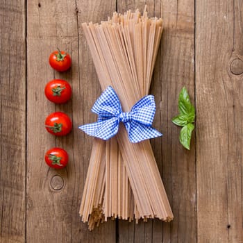 Pasta, tomatoes and basil on wooden background