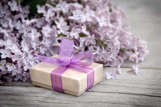 Gift box with purple bow and lilac on wood