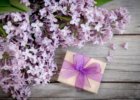 Gift box with purple bow and lilac on wood
