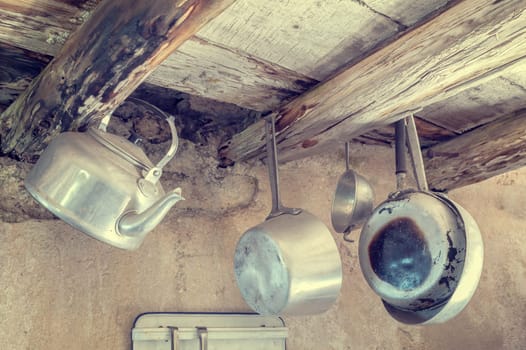 Old kitchen utensils in aluminum. Hanging from old wooden beams, pans, strainer, kettle.  Photo in styles vintage