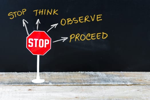 Mini STOP sign as Stop, Think, Observe and Proceed, hand drawing over chalkboard
