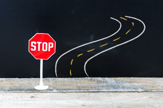 Mini STOP sign in front of curved road, hand drawing over chalkboard