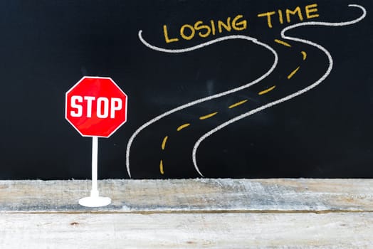 Mini STOP sign on the road to LOSING TIME, hand drawing over chalkboard