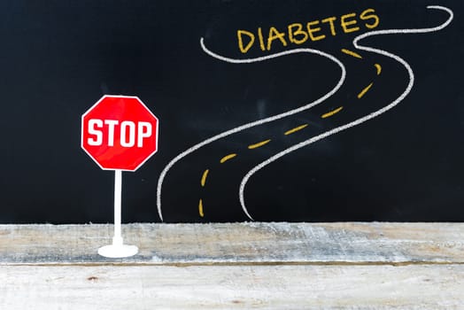 Mini STOP sign on the road to DIABETES, hand drawing over chalkboard