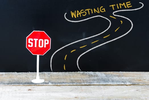 Mini STOP sign on the road to WASTING TIME, hand drawing over chalkboard