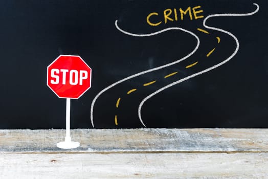 Mini STOP sign on the road to CRIME, hand drawing over chalkboard