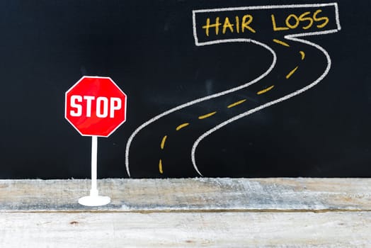 Mini STOP sign on the road to HAIR LOSS, hand drawing over chalkboard