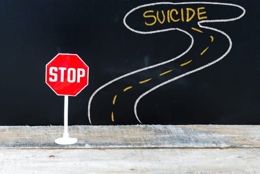 Mini STOP sign on the road to SUICIDE, hand drawing over chalkboard