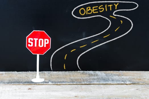 Mini STOP sign on the road to OBESITY, hand drawing over chalkboard