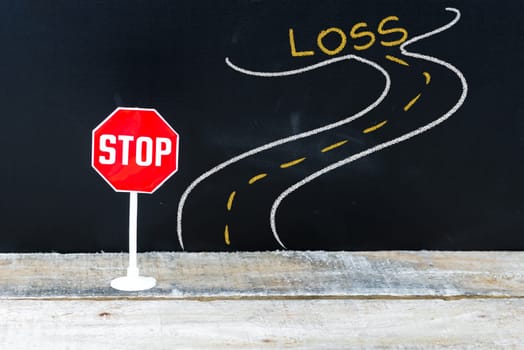 Mini STOP sign on the road to LOSS, hand drawing over chalkboard