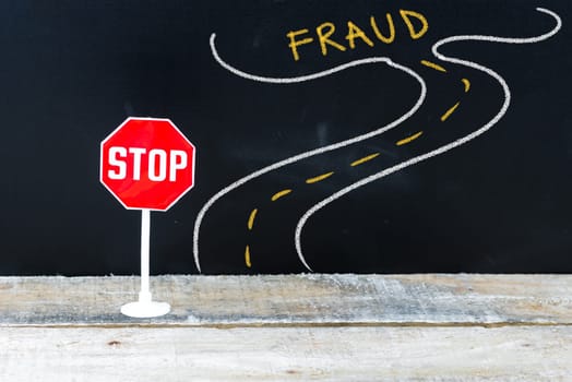 Mini STOP sign on the road to FRAUD, hand drawing over chalkboard