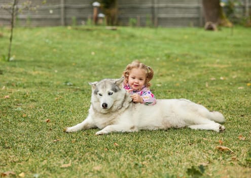 The little baby girl playing with dog against green grass in park