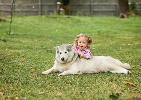 The little baby girl playing with dog against green grass in park