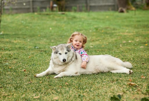 The little baby girl playing with dog against green grass in park