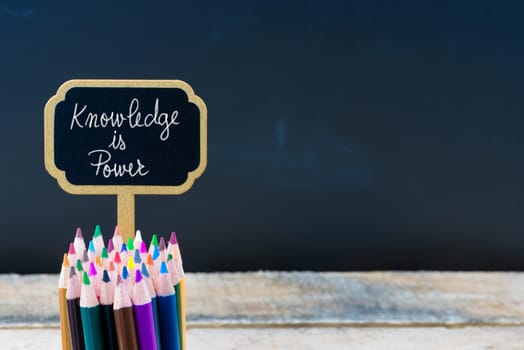 Wooden mini blackboard label with message Knowledge is Power and colouring pencils over chalkboard background, copy space available, education concept